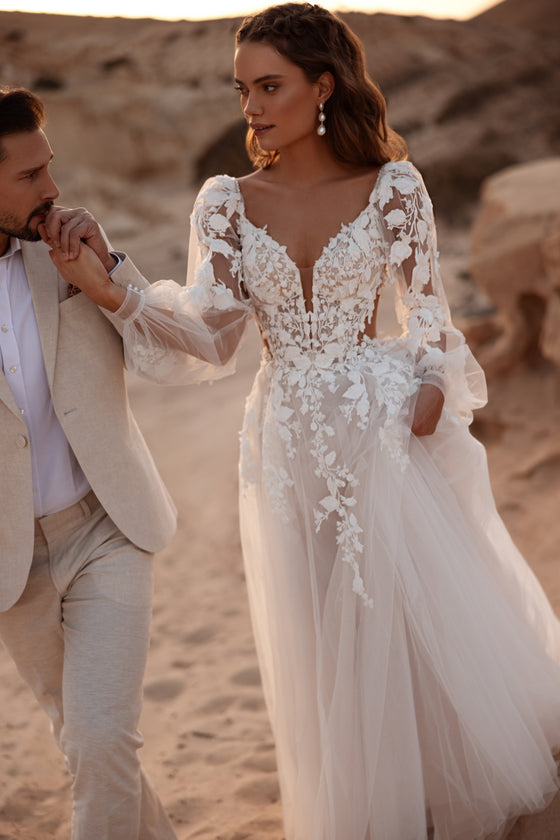 L’abito da sposa Alia ha un corpetto aderente a corsetto in pizzo, con applicazioni floreali 3D e un profondo scollo a V, che definisce con eleganza la vita.