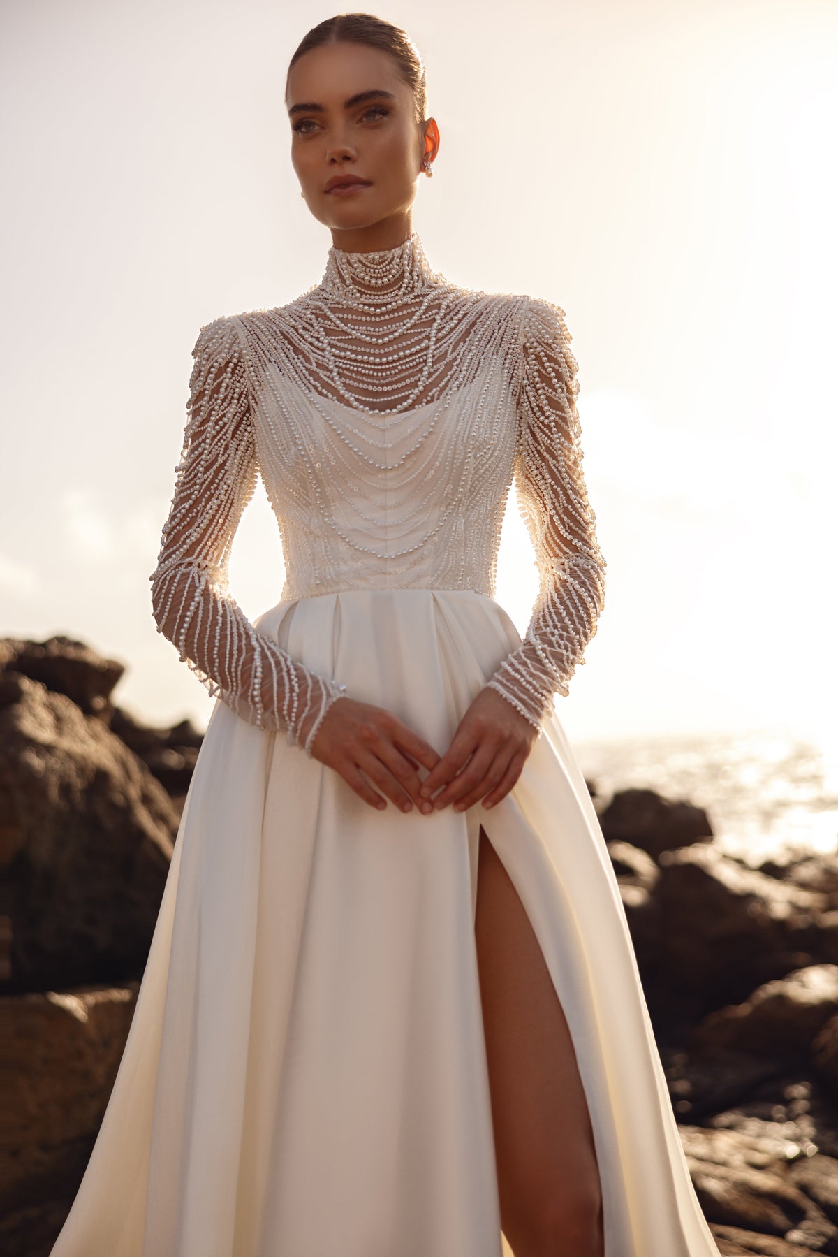 La blusa da sposa Alya, con lunghe maniche decorate con perle, abbinata a una gonna con spacco alto, esprime un look contemporaneo e prezioso.
