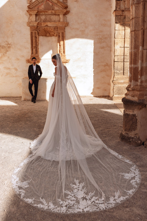 Il velo da sposa cattedrale Ariella, bordato di pizzo, aggiunge un accento scenografico e senza tempo, per cerimonie eleganti.