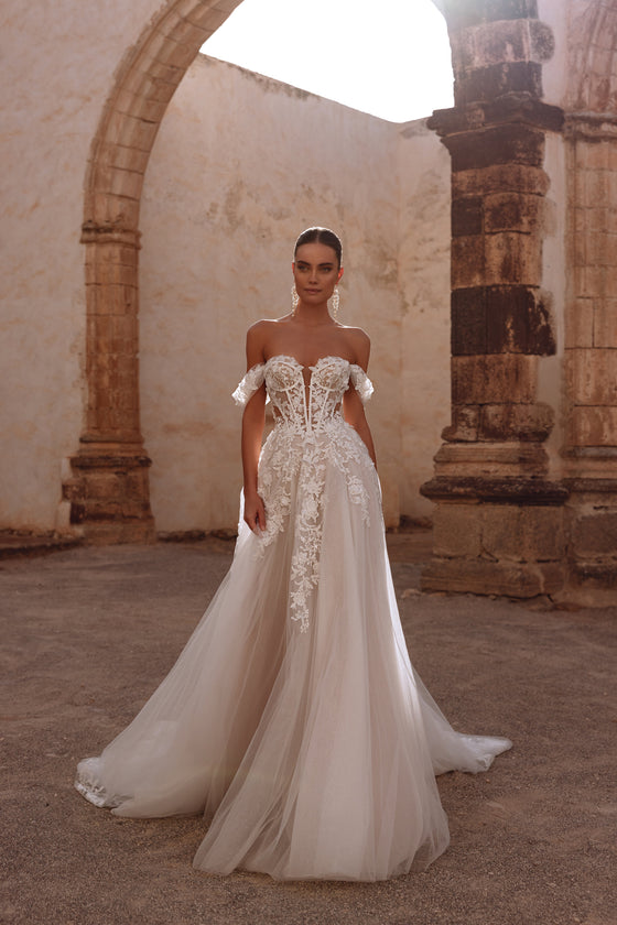 L’abito da sposa Ariella ha un corsetto con stecche a vista e intricate applicazioni di pizzo floreale, per un’eleganza delicata ed eterea.