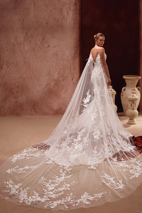 La cappa da sposa Aspasia in morbido tulle, con applicazioni floreali 3D, aggiunge all’abito un accento scenografico e romantico.