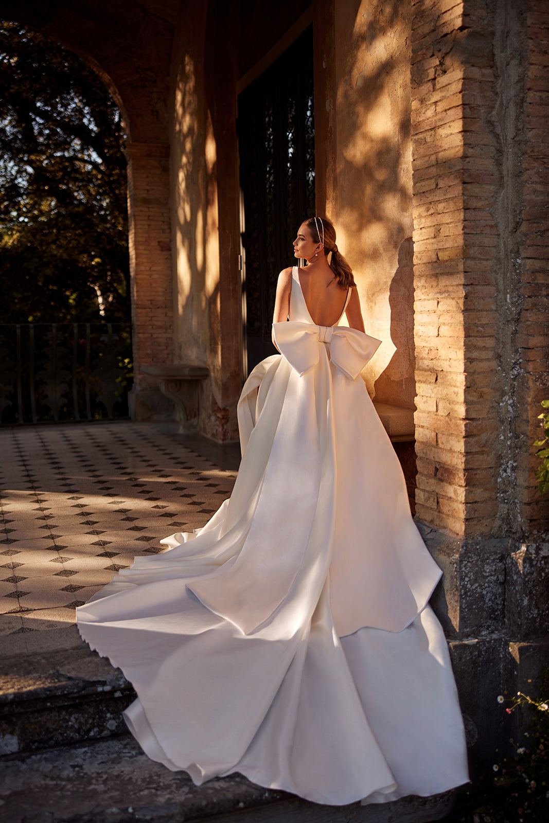 Abito da sposa classico Margo con strascico a fiocco di DAMA Couture (vista posteriore nella foto della campagna)