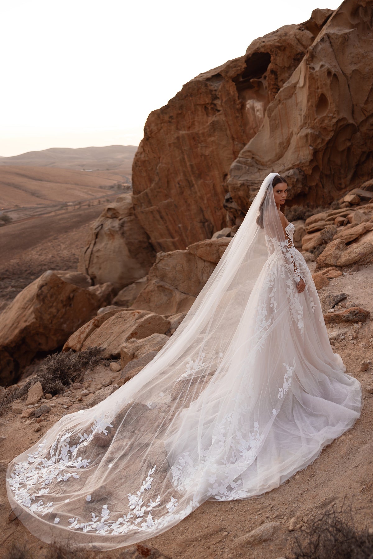 L’abito da sposa Nabila, con maniche in pizzo e corpetto a corsetto strutturato, sottolinea uno stile romantico e contemporaneo.