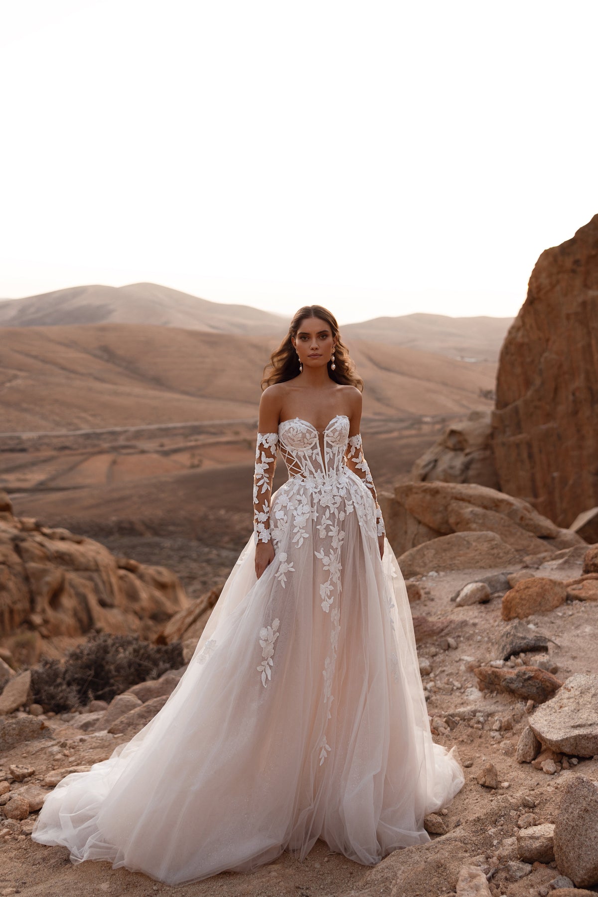 L’abito da sposa Nabila, con lungo velo cattedrale e maniche in pizzo, esprime eleganza senza tempo e preziosa lavorazione artigianale.