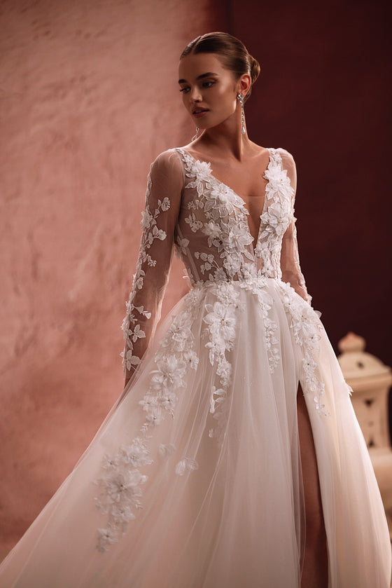 L’abito da sposa Semiramida ha un corsetto trasparente con ricami floreali e applicazioni tridimensionali, per un’estetica romantica e leggera.