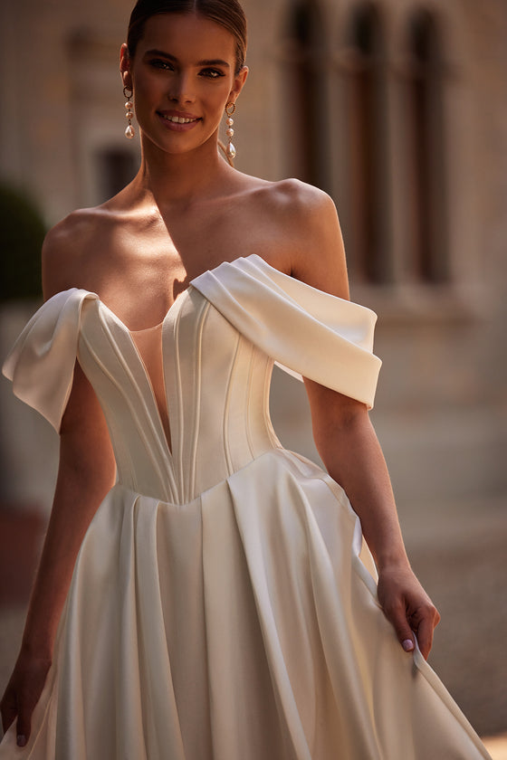 Abito da sposa Thalia classico ed essenziale, con maniche che scendono dalle spalle, di DAMA Couture (foto principale)