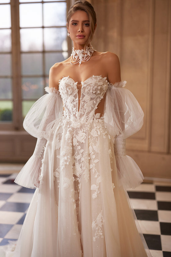 Abito da sposa Estella – abito da sposa a trapezio con un corsetto con fiori in rilievo e voluminose maniche che lasciano le spalle scoperte.