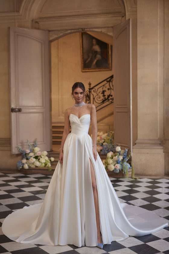 Abito da sposa Lucienne – abito da sposa a trapezio con uno scollo effetto illusion decorato di cristalli e una gonna drappeggiata in raso con spacco alto.