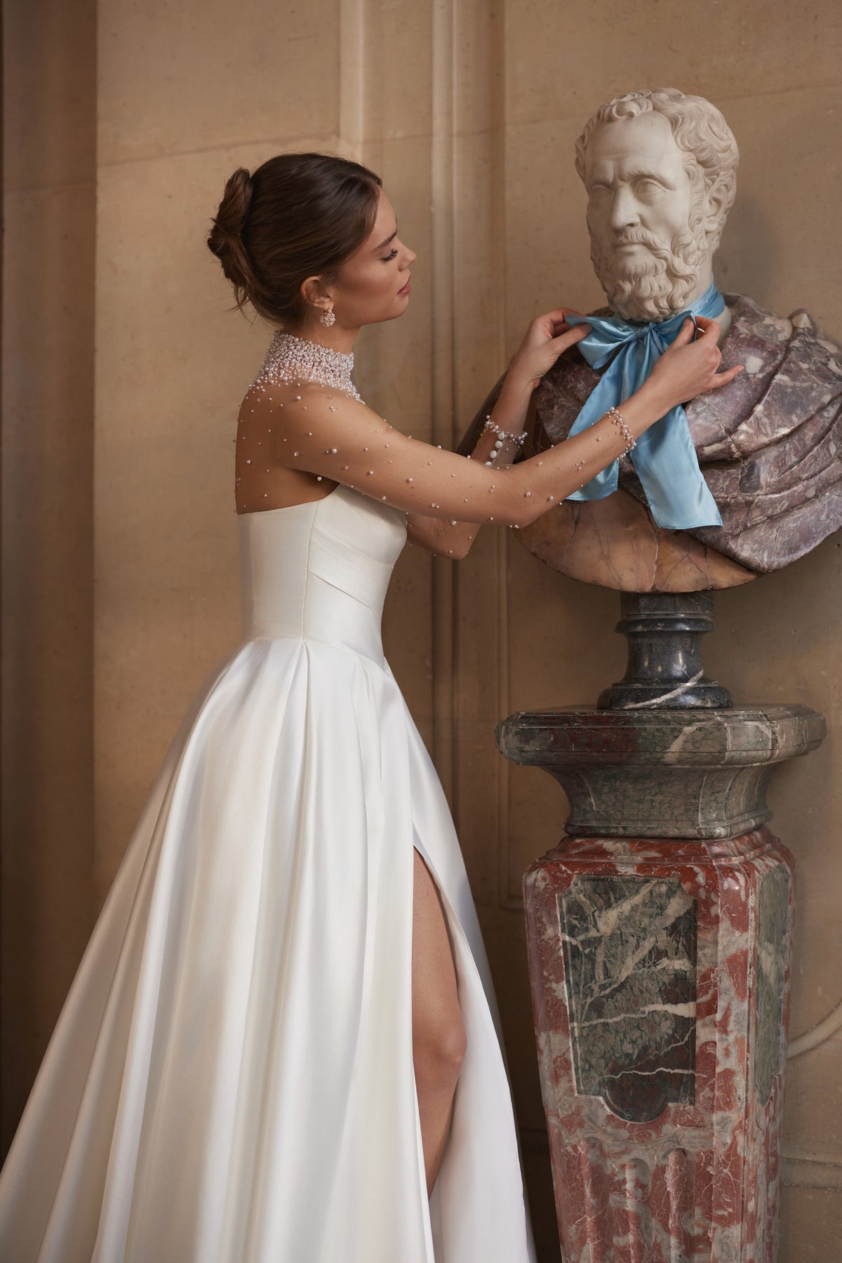 Abito da sposa Lucienne – uno scollo effetto illusion decorato di cristalli e una gonna drappeggiata in raso con spacco alto.