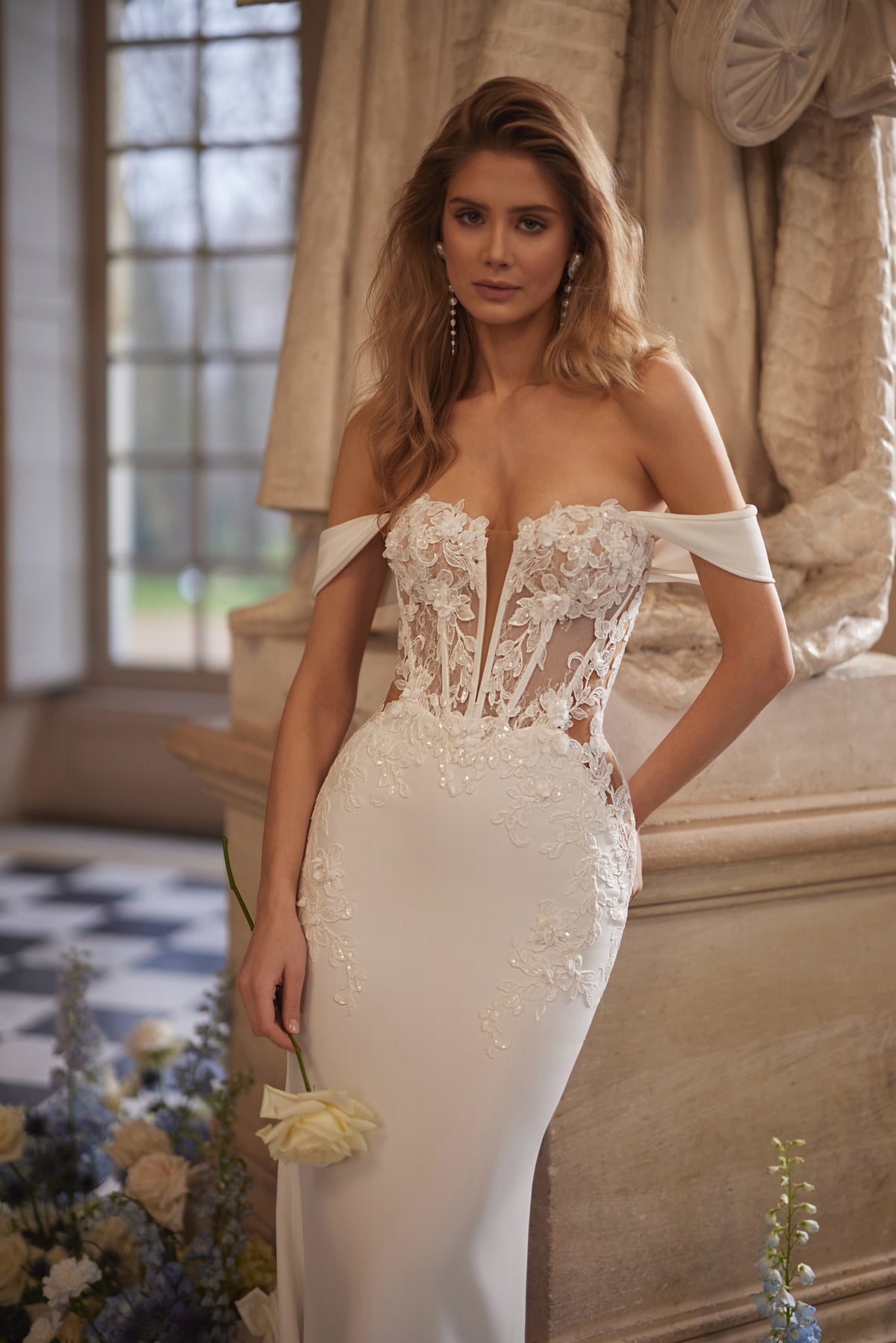 Abito da sposa Matilde – uno scollo che lascia le spalle scoperte e una silhouette aderente disegnata dal pizzo, DAMA Couture Something Blue 2027.