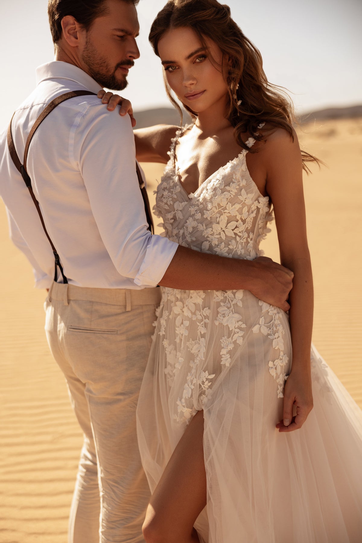 L’abito da sposa Aviva presenta un corpetto in pizzo trasparente con dettagli floreali 3D, che valorizza la figura nella luce del deserto.