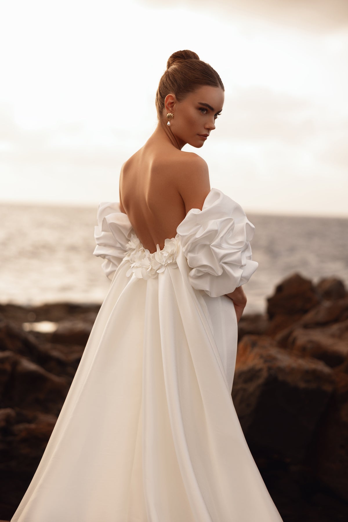 Abito da sposa con schiena scoperta, maniche a sbuffo e delicate applicazioni floreali, per un look d’ispirazione couture.