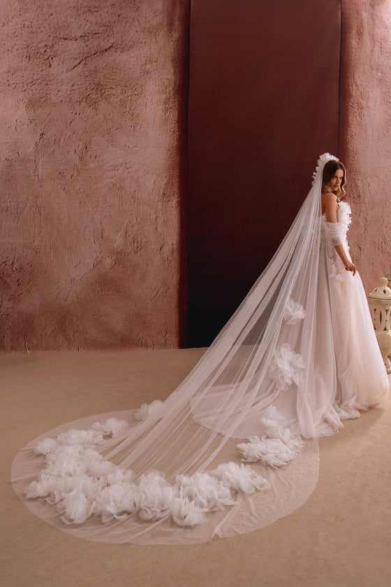 Lungo velo da sposa Bella con delicati fiori 3D sull’orlo, che aggiunge eleganza al look.