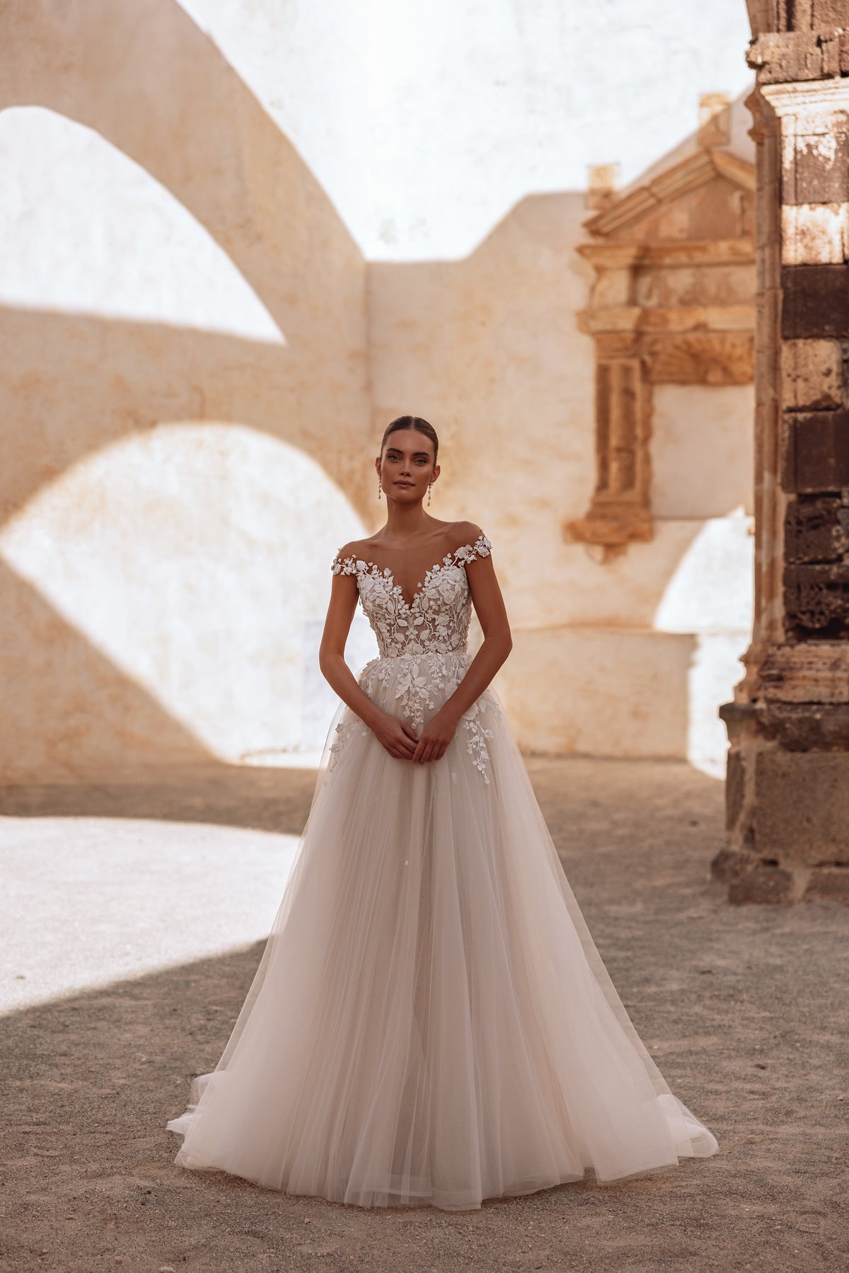 L’abito da sposa Andrea, con schiena scoperta e corpetto in pizzo, disegna una linea d’effetto completata da un morbido strascico in tulle.