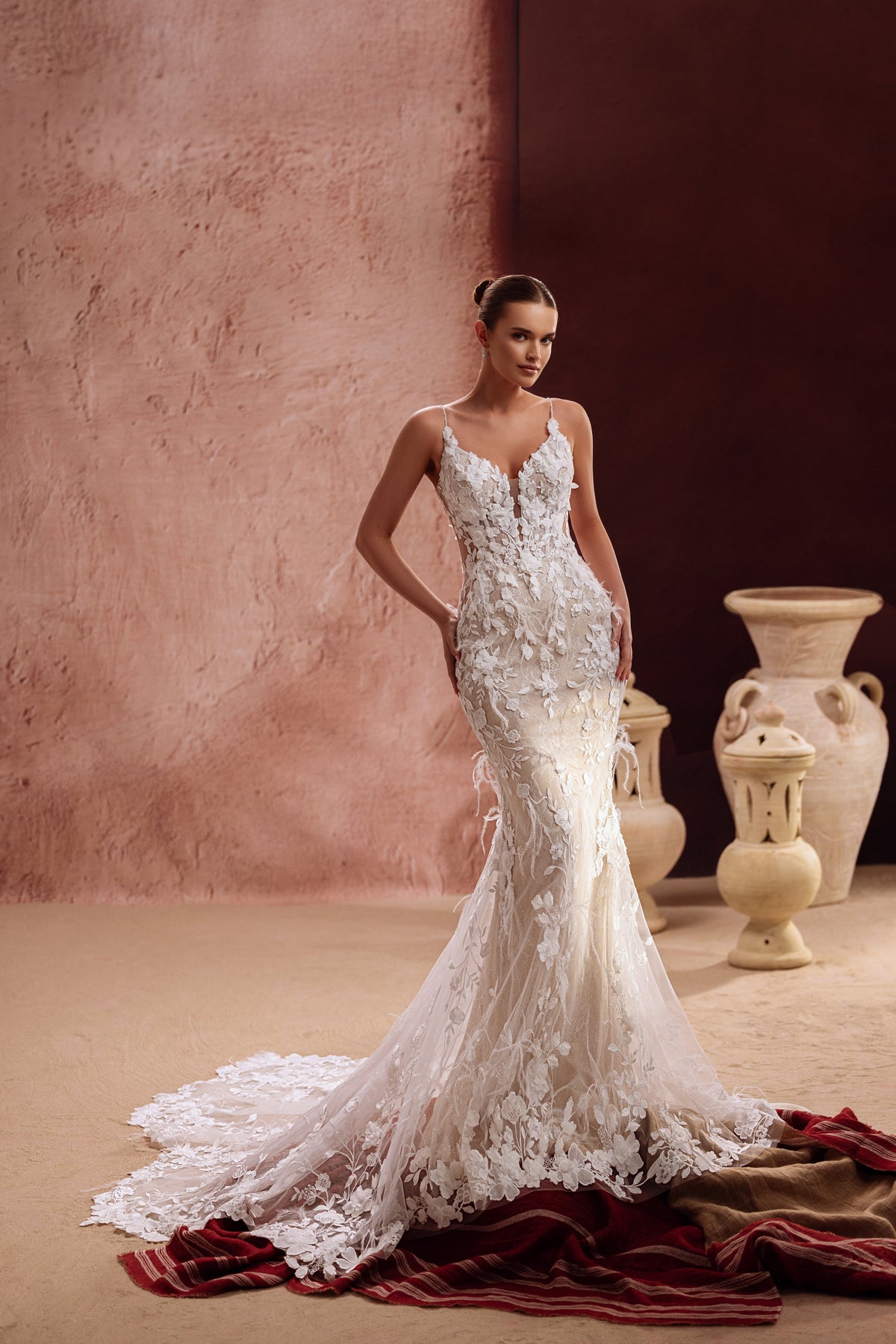 L’abito da sposa Aspasia unisce un corpetto in pizzo floreale a uno strascico fluido in tulle, per un look romantico e sognante.
