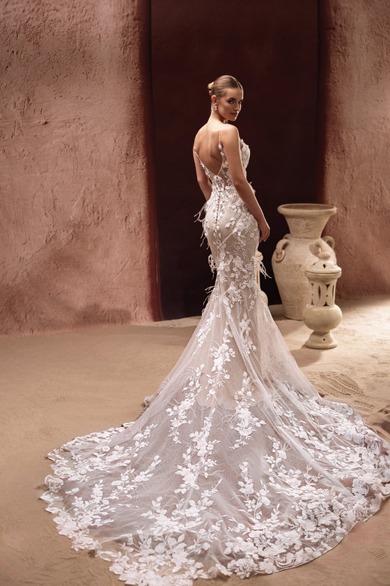 L’abito da sposa Aspasia presenta una profonda scollatura sulla schiena e uno strascico in pizzo ricamato, unendo sensualità e bellezza senza tempo.