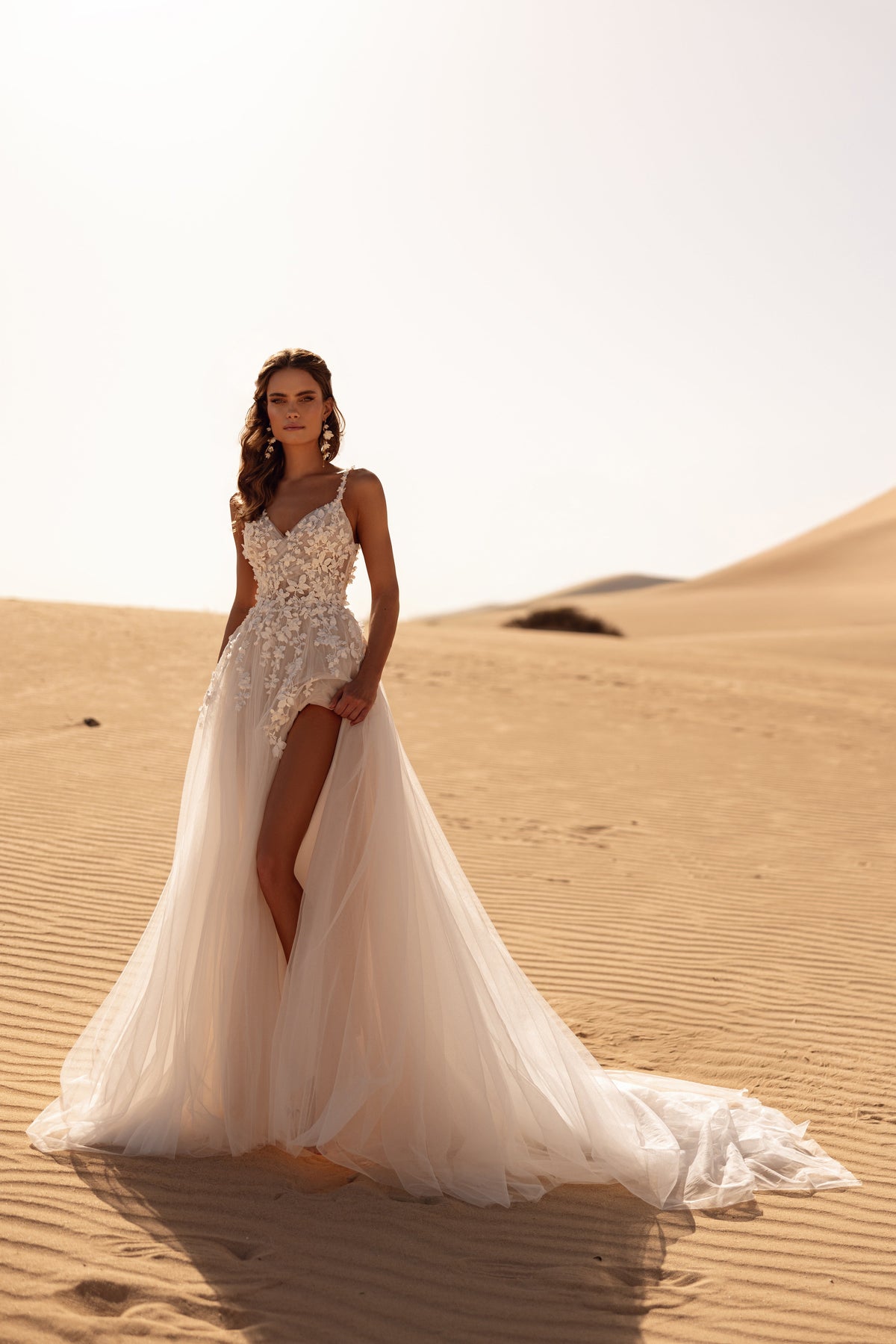 L’abito da sposa Aviva, con lungo strascico e velo fluido, crea un look d’effetto nella luce dorata del deserto.