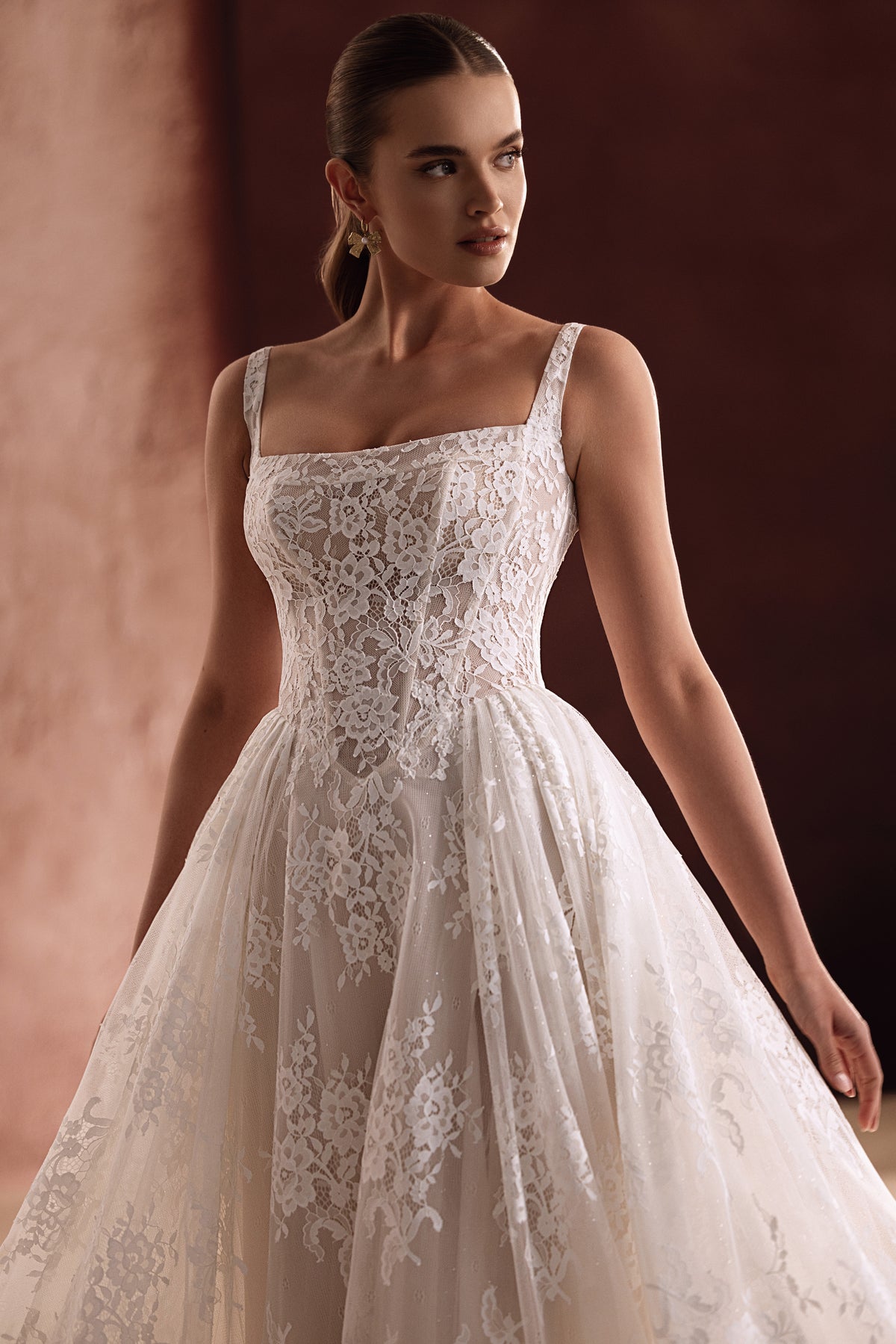 L’abito da sposa Becco, con scollo quadrato e ricchi dettagli in pizzo, valorizza la figura con eleganza raffinata.