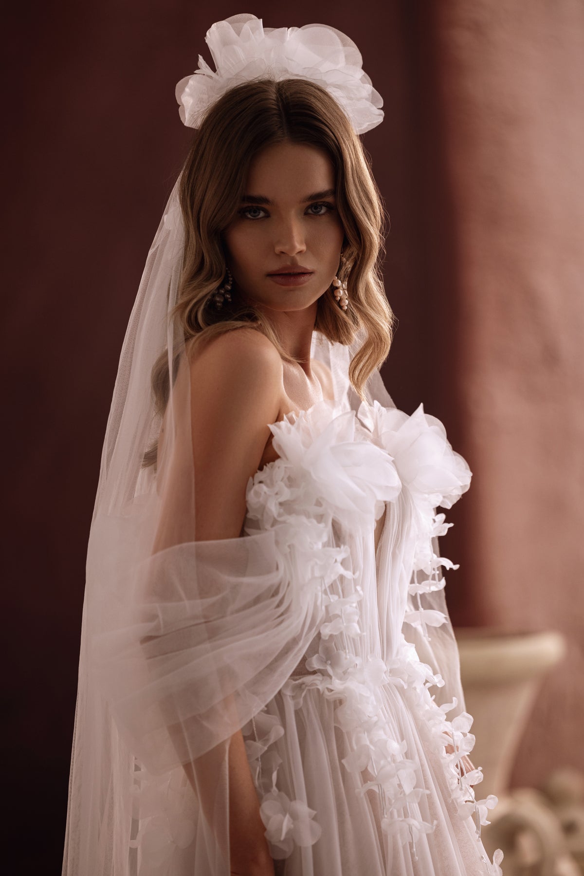 L’abito da sposa Bella, con spacco fino alla coscia e applicazioni floreali, unisce eleganza sensuale e leggerezza romantica.