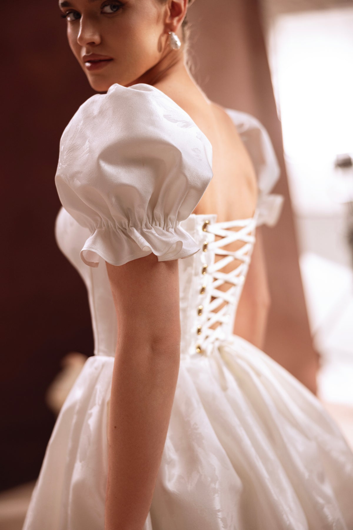 L’abito da sposa corto Daphne, con scollo a cuore e maniche a sbuffo, esprime grazia femminile e fascino contemporaneo.
