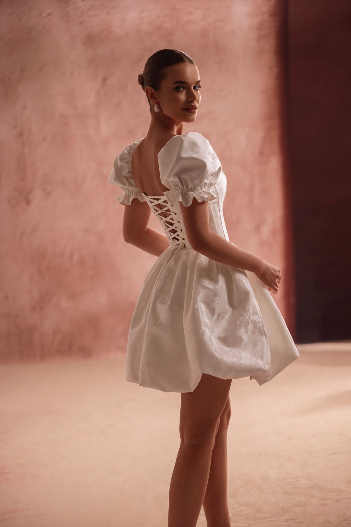 L’abito da sposa mini Daphne, con corsetto allacciato sulla schiena e maniche a sbuffo, sottolinea la vita e propone un giocoso look da principessa.