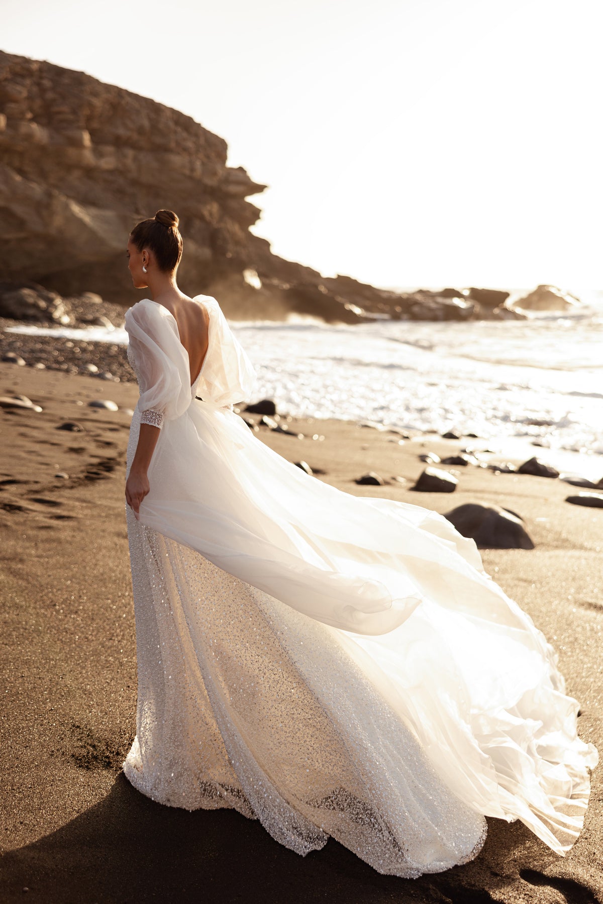 L’abito da sposa Davina mostra uno scenografico strascico in tulle e la schiena scoperta, per una linea romantica e leggera.