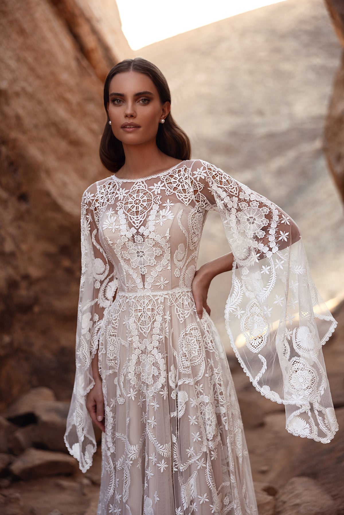 L’abito da sposa Dune presenta uno scenografico strascico in pizzo e maniche svasate, per una sposa boho-chic nel deserto.