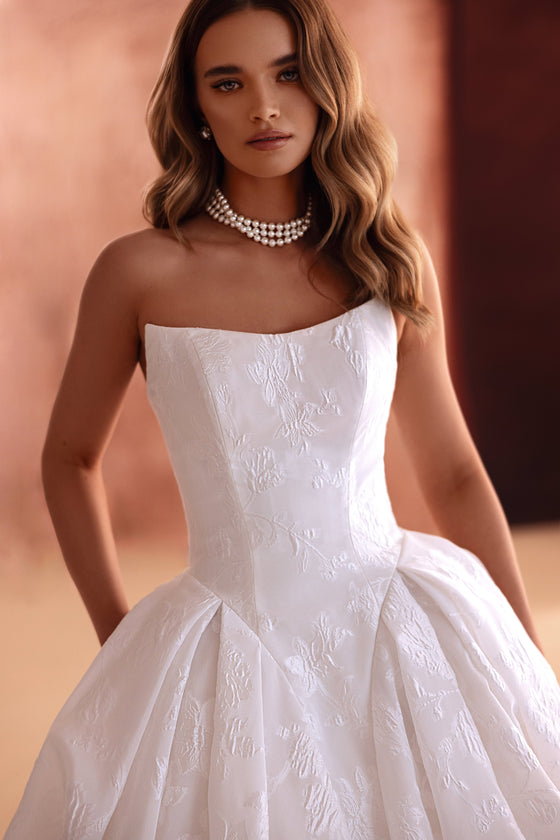 L’abito da sposa Hebe presenta una linea a principessa senza spalline in jacquard floreale, per un look senza tempo.