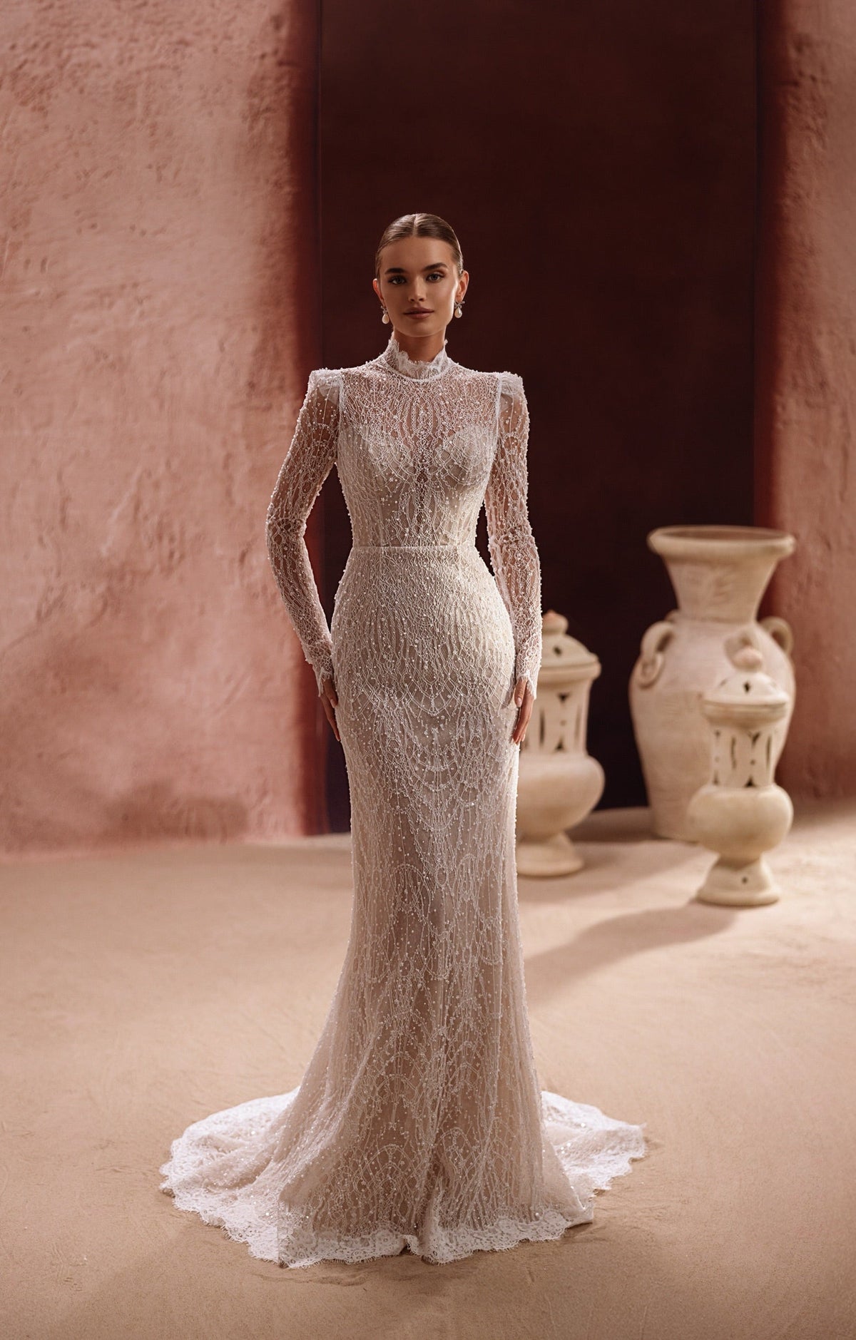 L’abito da sposa Henriette presenta un corpetto in pizzo a collo alto, con maniche lunghe e delicate perline, per un’eleganza senza tempo.