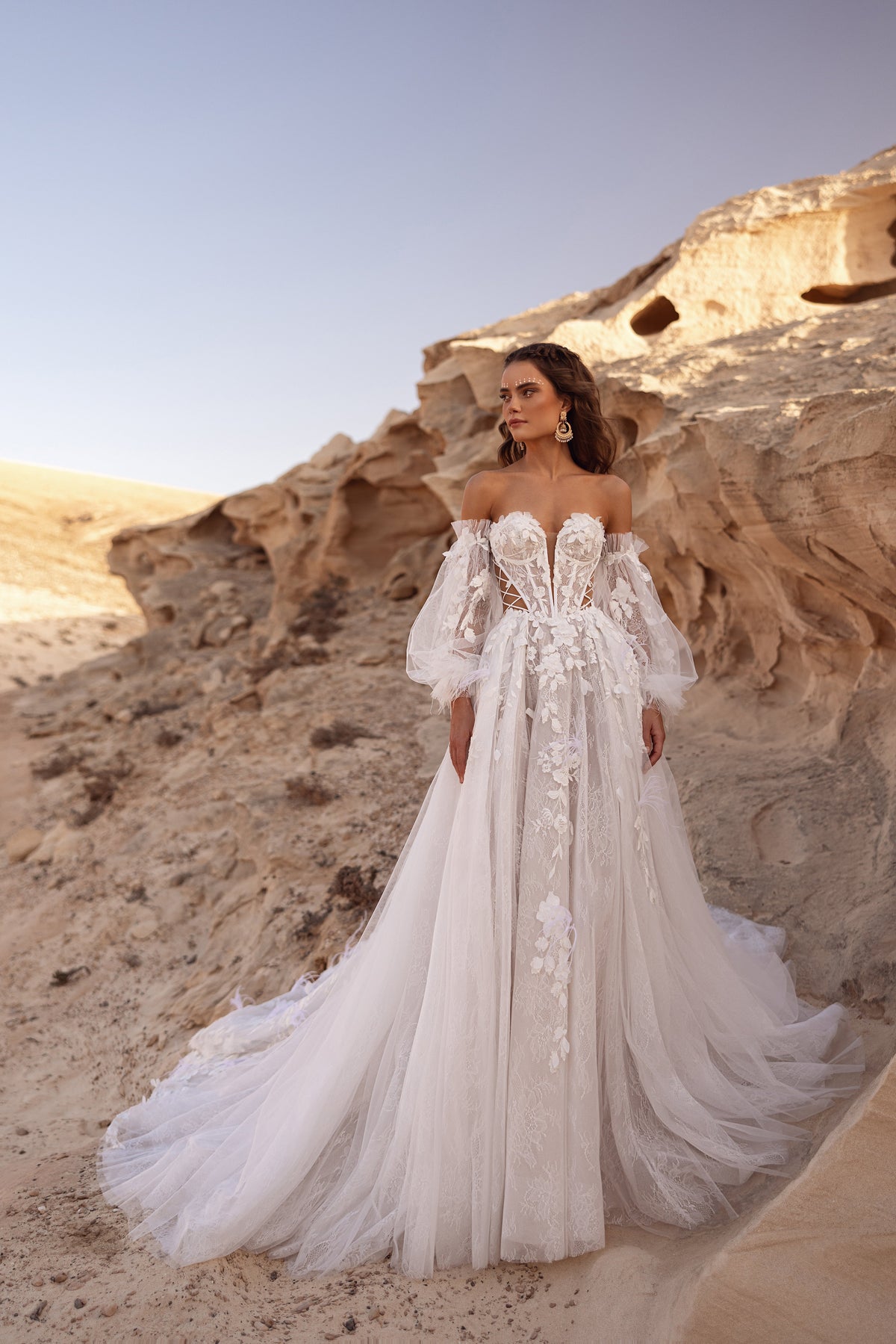 L’abito da sposa Huda presenta un corsetto a spalle scoperte con applicazioni floreali 3D e allacciatura laterale, per un look boho contemporaneo.