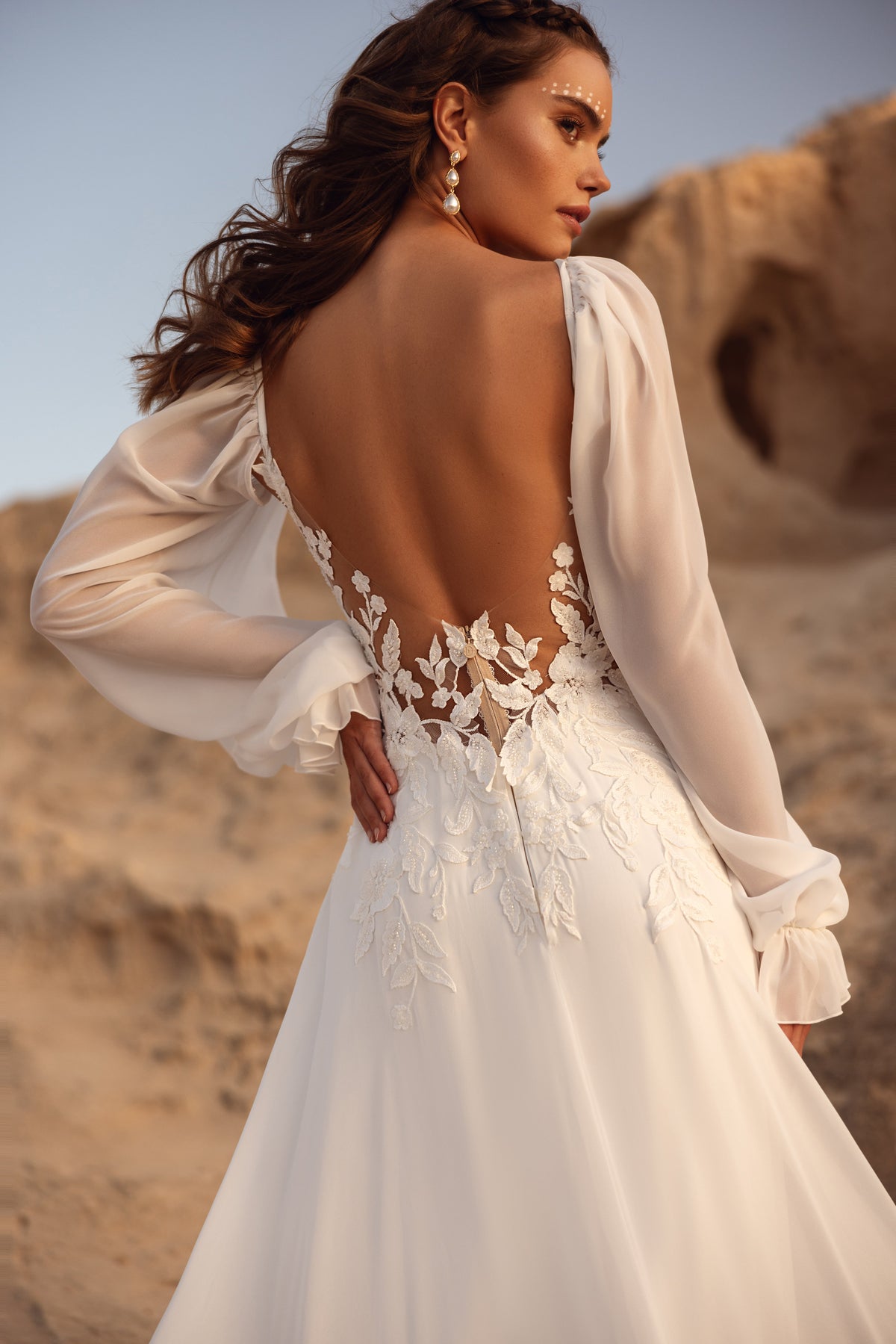 L’abito da sposa Judith, con corpetto in pizzo trasparente e maniche ampie e morbide, unisce spirito boho ed eleganza raffinata.