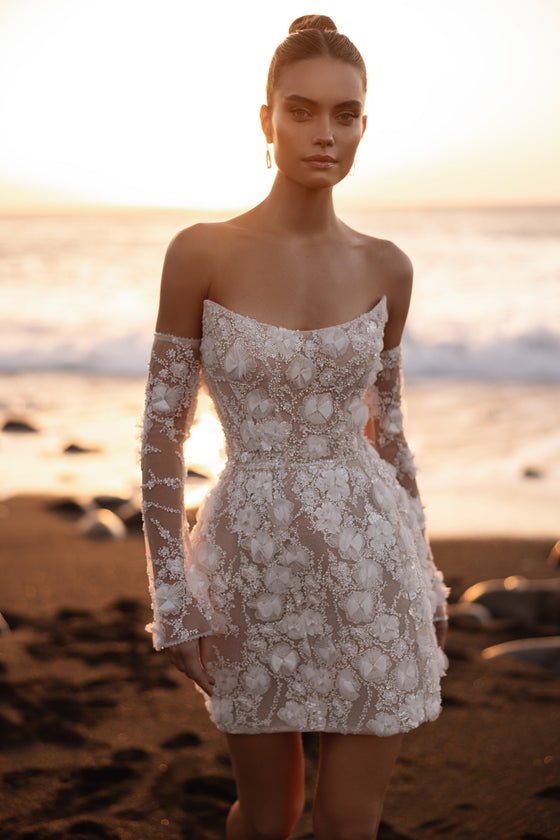 L’abito da sposa Kayla presenta maniche che lasciano scoperte le spalle e ricchi ricami floreali 3D, per un romantico matrimonio sulla spiaggia.