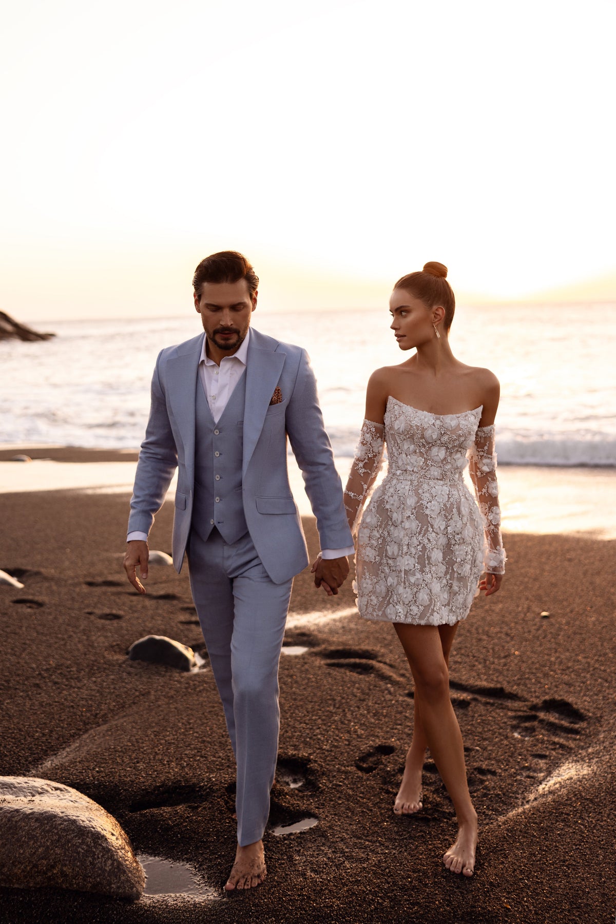 L’abito da sposa corto Kayla, con maniche lunghe trasparenti e applicazioni floreali 3D, rilegge in chiave contemporanea uno stile senza tempo.