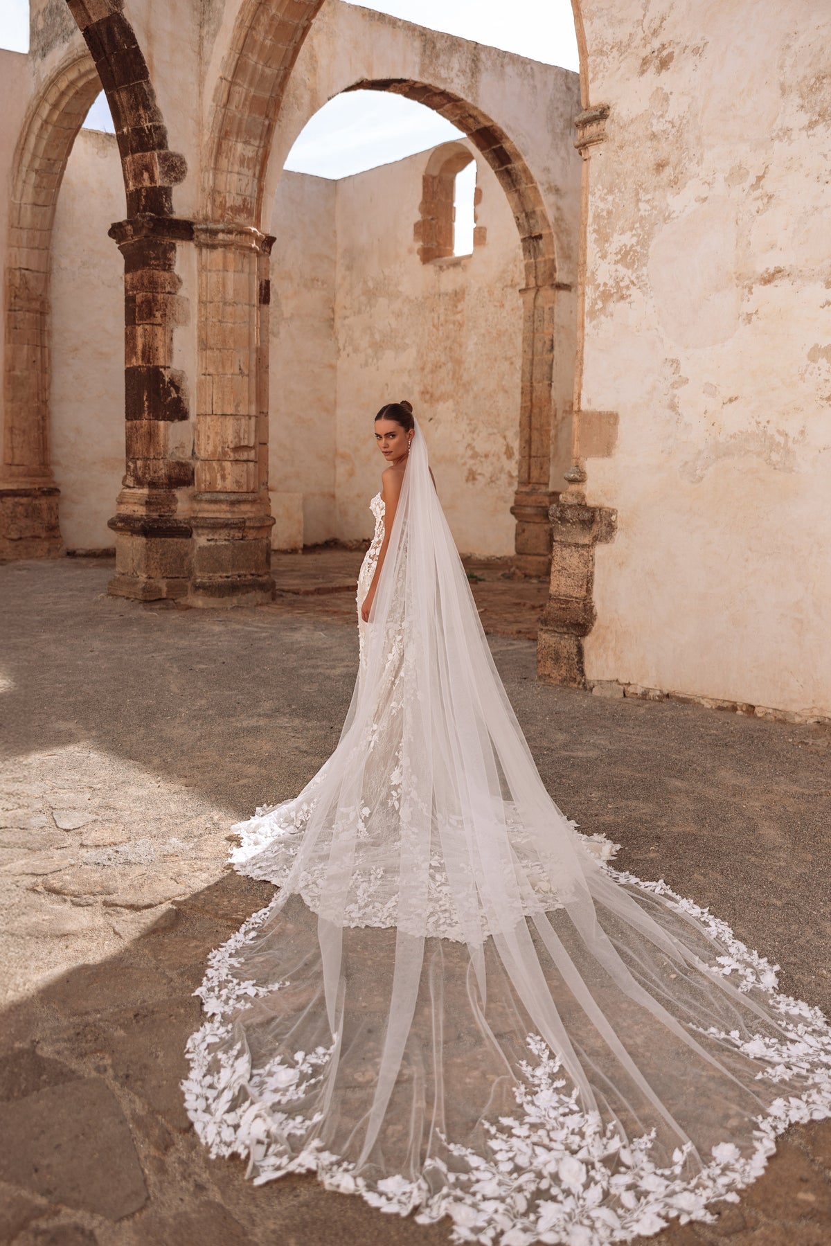 Abito da sposa in pizzo con velo di lunghezza cattedrale e strascico con applicazioni floreali, per un look senza tempo.