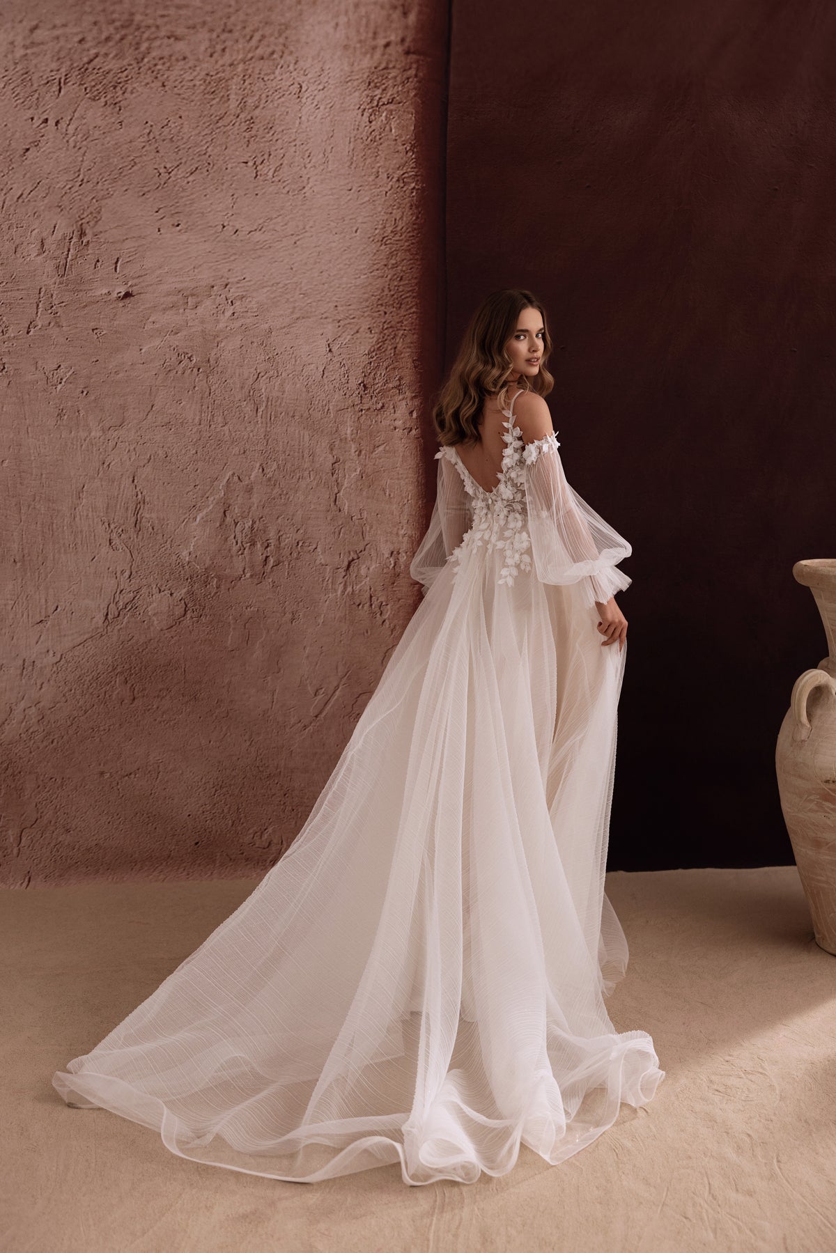 L’abito da sposa Lilibeth, con spalle scoperte e morbido strascico, esprime un fascino etereo e un romanticismo disinvolto.