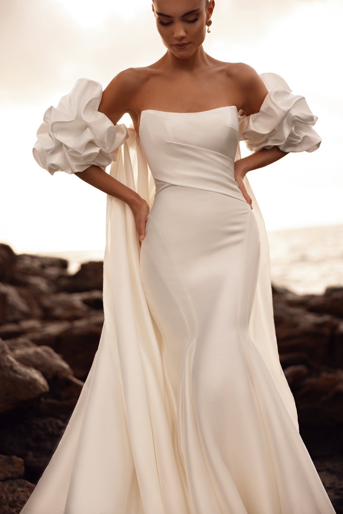 Abito da sposa a sirena, con maniche a sbuffo che lasciano scoperte le spalle e corpetto strutturato che valorizza la vita.