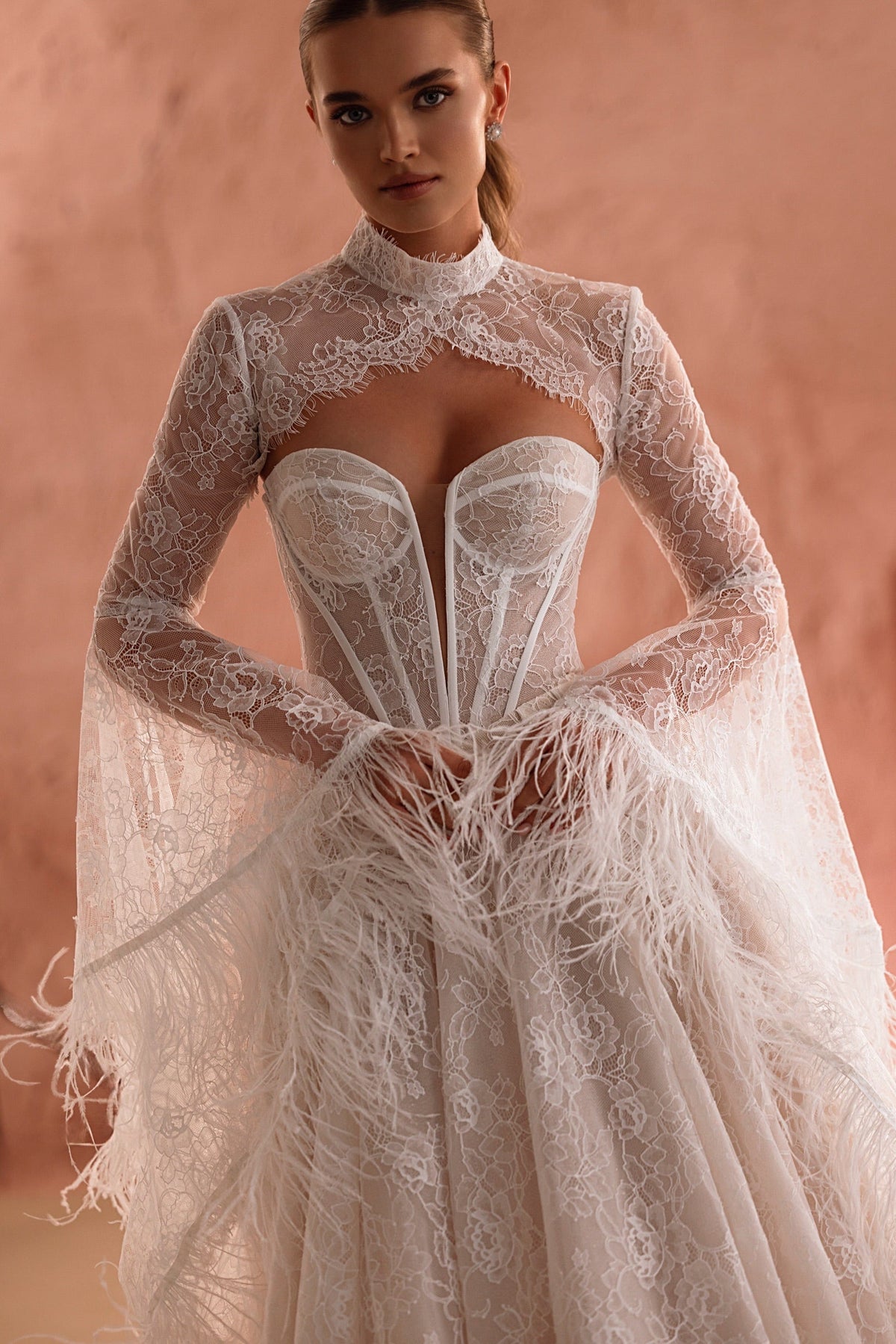 Il bolero da sposa Michelle, con dettagli in pizzo e maniche con piume, è un elemento di carattere per una sposa contemporanea.