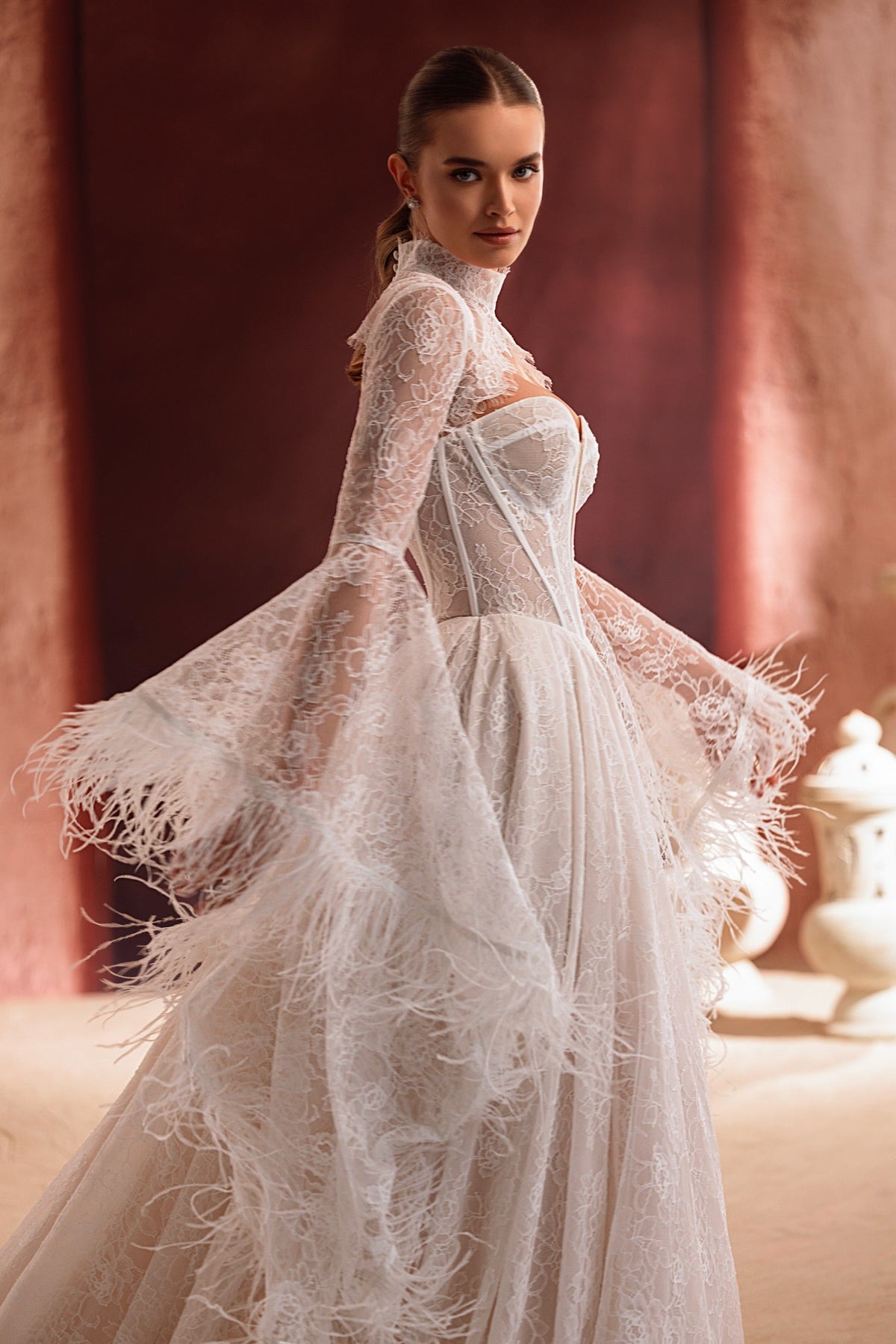 L’abito da sposa Michelle, con scenografiche maniche a campana e accenti di piume, propone uno stile deciso d’ispirazione couture.