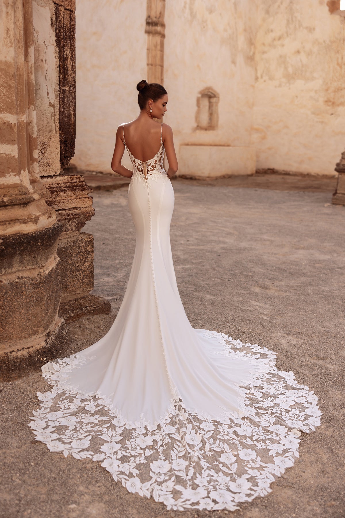 L’abito da sposa Munira, con linea aderente e strascico in pizzo, unisce eleganza classica e fascino contemporaneo.