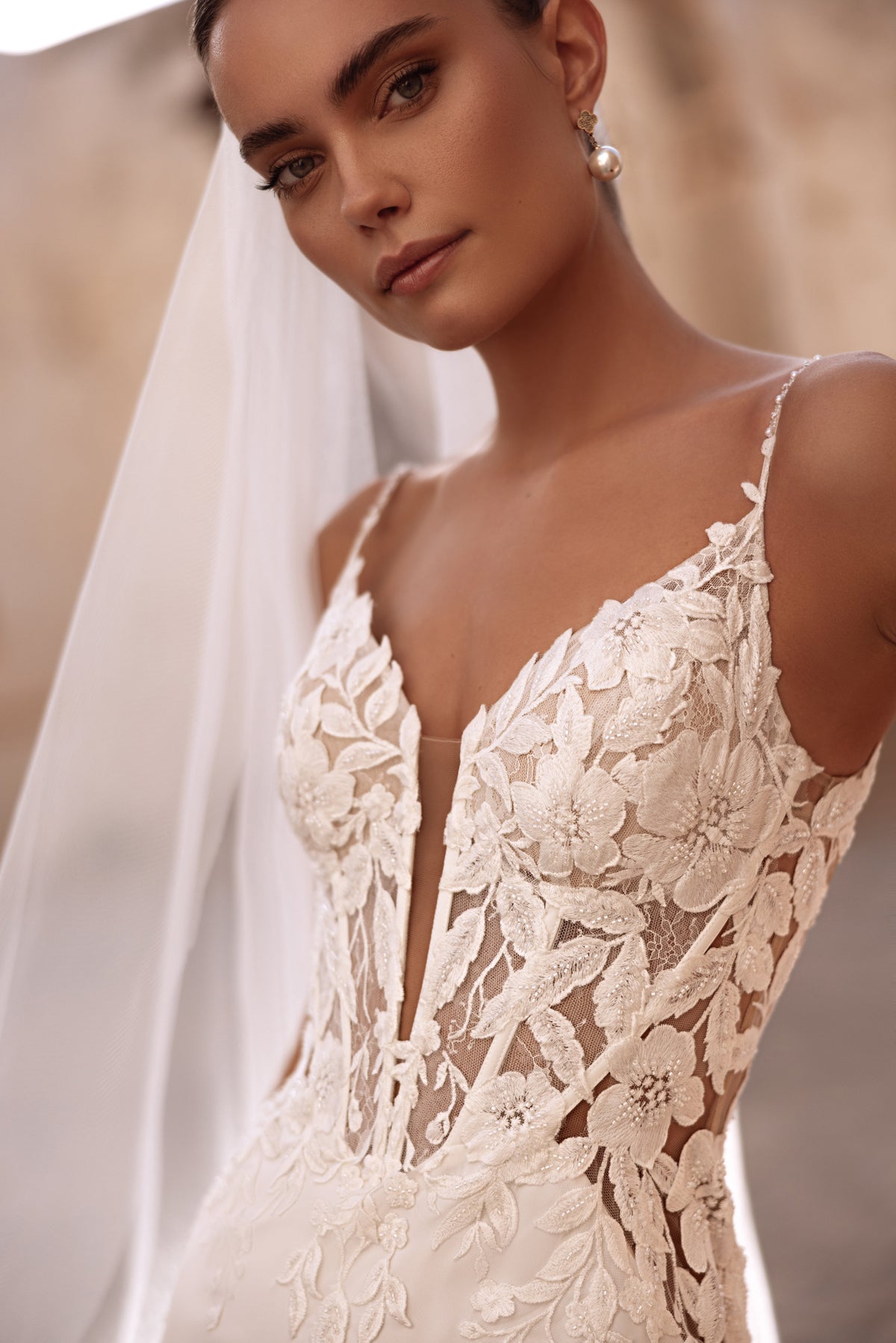 L’abito da sposa Munira in pizzo presenta applicazioni floreali 3D e inserti trasparenti, per un look contemporaneo e romantico.