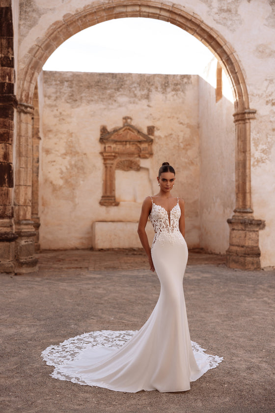 L’abito da sposa Munira presenta un corpetto in pizzo con profondo scollo a V e ricami elaborati, abbinato a una linea a sirena aderente.