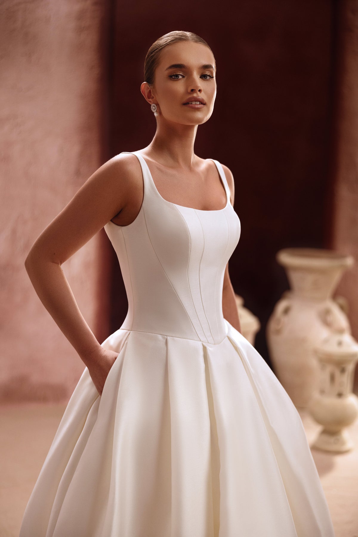 L’abito da sposa Nicolette presenta un corpetto essenziale in raso con spalline e una voluminosa gonna a principessa, per un look senza tempo.