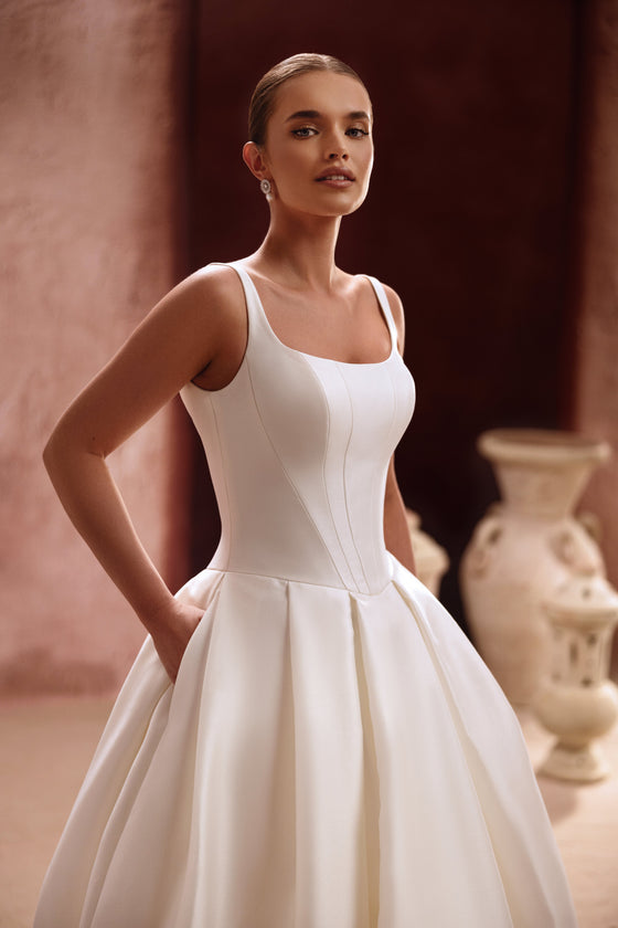L’abito da sposa Nicolette presenta un corpetto essenziale in raso con spalline e una voluminosa gonna a principessa, per un look senza tempo.