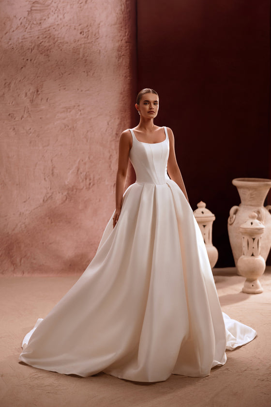 L’abito da sposa Nicolette, con scollo quadrato e corpetto strutturato, valorizza la figura con un’eleganza disinvolta.
