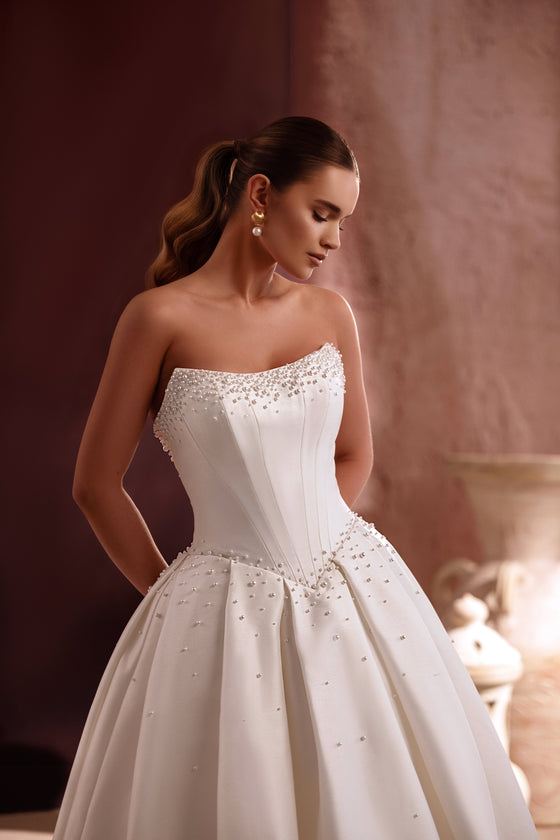L’abito da sposa Noor a principessa in raso, con corsetto senza spalline e decorazioni di perle, esprime un’eleganza senza tempo.