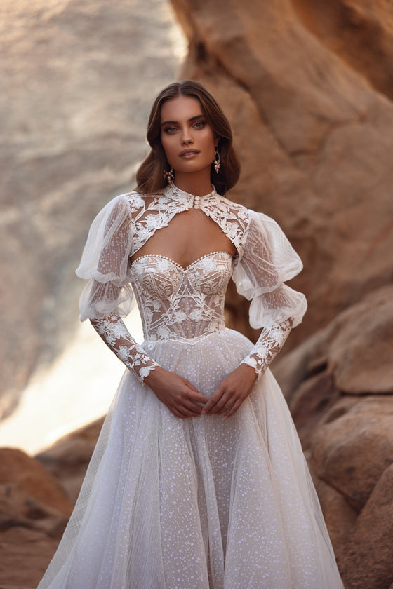 L’abito da sposa Oasis in pizzo, con maniche a sbuffo e gonna in tulle trasparente, unisce romanticismo vintage ed eleganza d’ispirazione couture.
