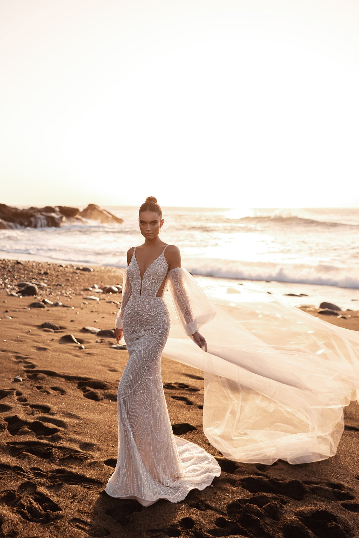 L’abito da sposa Rebecca, con ricami di perle e maniche in tulle che lasciano scoperte le spalle, unisce scintillii delicati e un disegno sensuale.