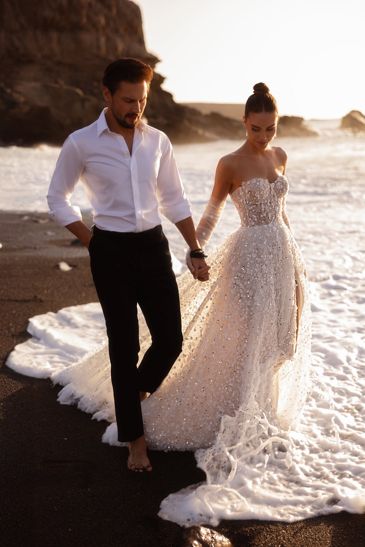 L’abito da sposa Reem, con corsetto ricamato con perline e spacco anteriore, brilla di migliaia di paillettes, per un look d’effetto sulla spiaggia.
