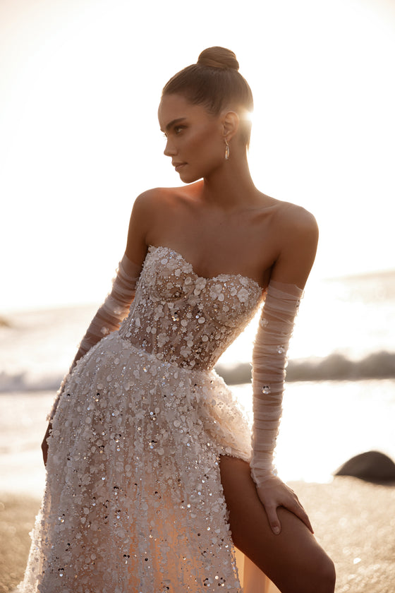 L’abito da sposa Reem, con corpetto a corsetto e spacco alto, risplende di ricami floreali 3D e dettagli scintillanti nella luce dorata del tramonto.