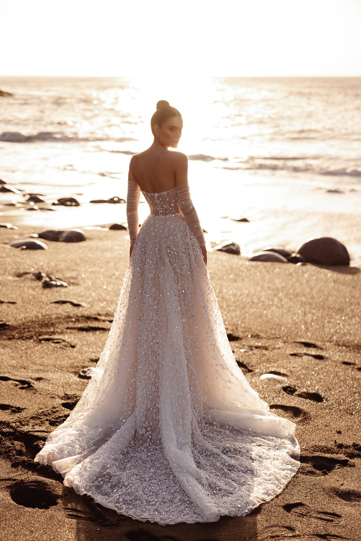 L’abito da sposa Reem, con corsetto effetto illusion e decorazioni floreali 3D, valorizza l’eleganza femminile nella luce del tramonto.